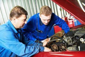 AAMCO Utah Diagnostic Services Two mechanics are working on a red car in a garage.