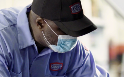 A man wearing a mask and an AAMCO shirt
