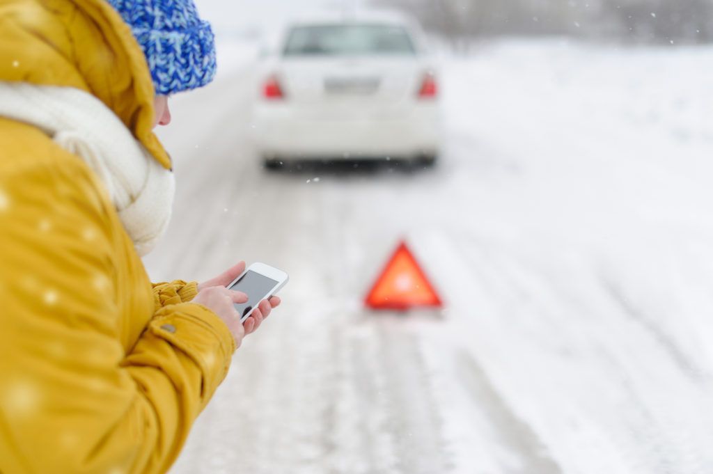 A woman is using a cell phone to call a tow truck.