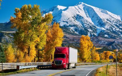 A red semi truck is driving down a mountain road.
