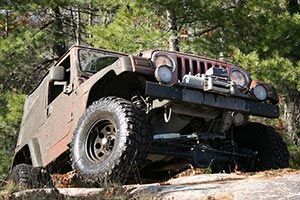 A jeep is parked on a rocky hillside in the woods.