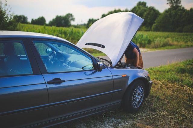 A man is looking under the hood of a broken down car.