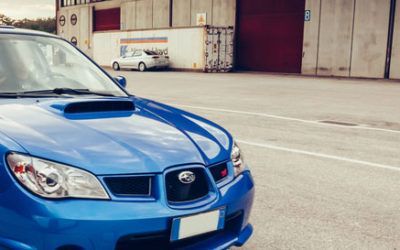 A blue subaru is parked in a parking lot in front of a building.