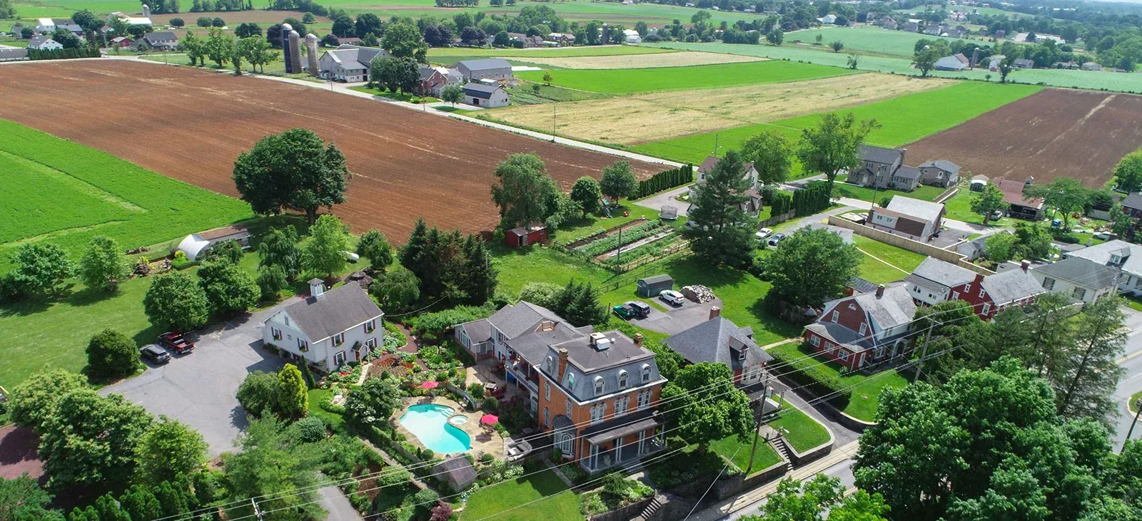 An aerial view of a house with a pool in the middle of a lush green field.