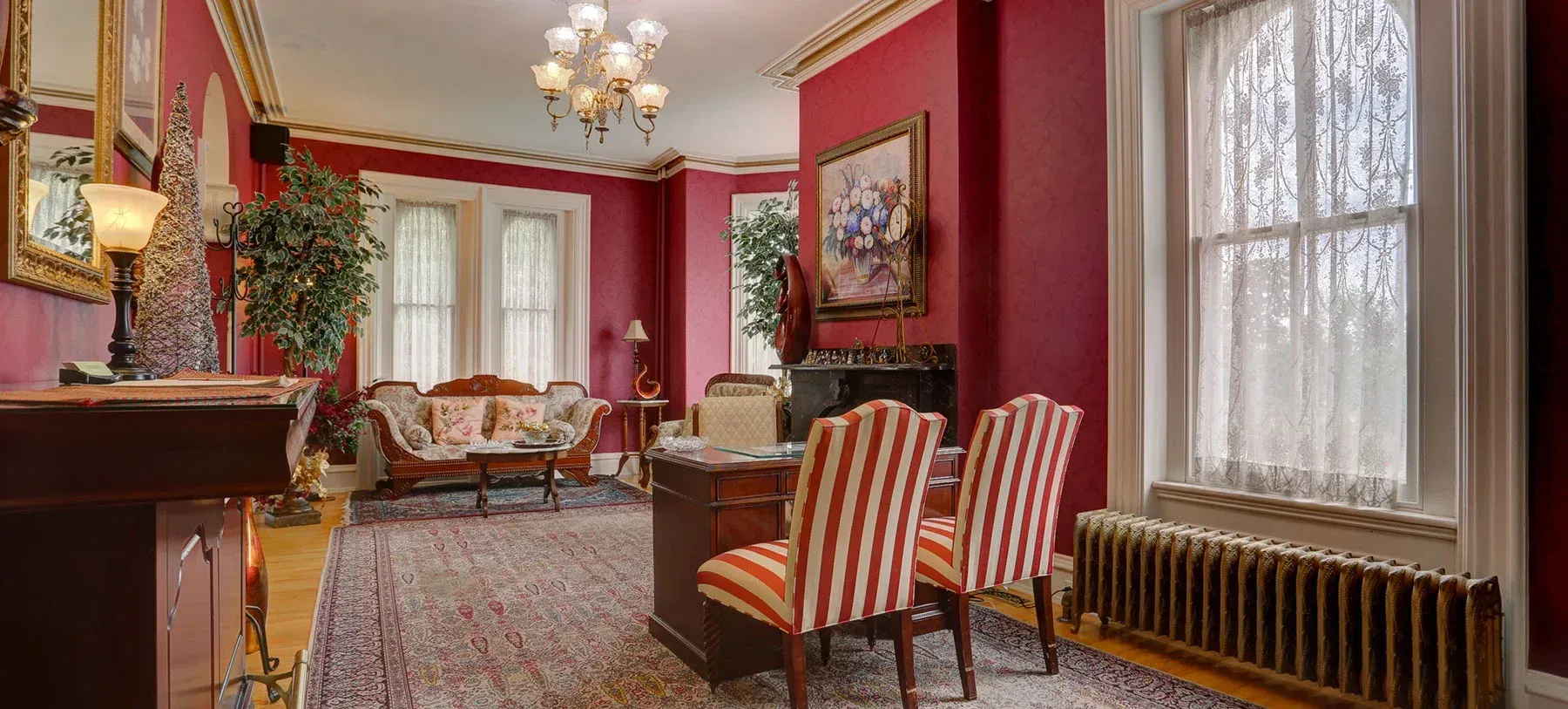 A living room with red walls , a couch , chairs , a desk and a fireplace.