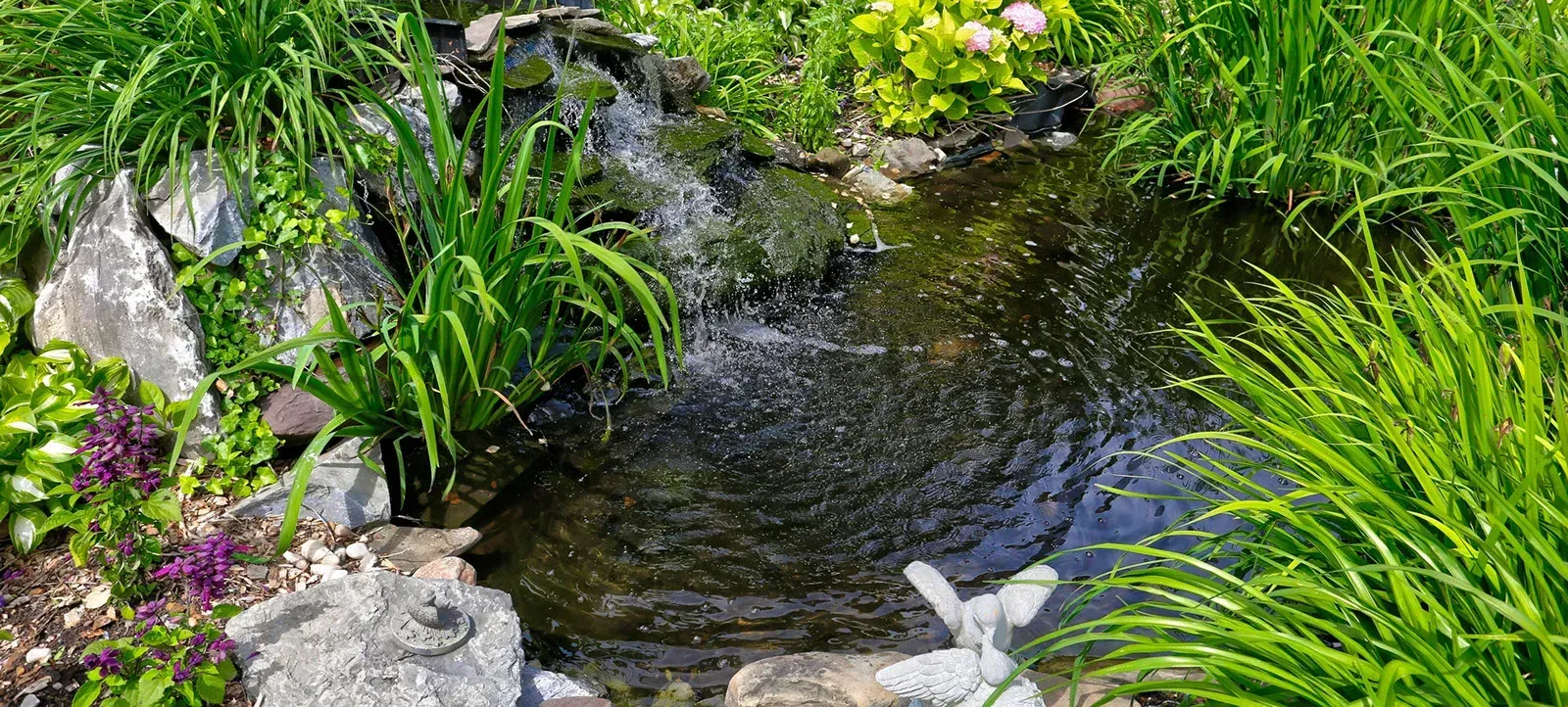 A small waterfall in a garden surrounded by plants and rocks.
