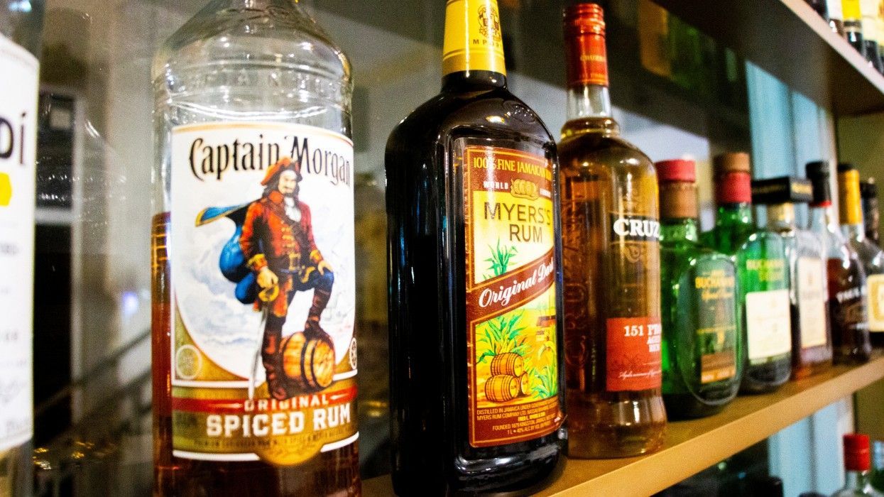 A shelf filled with bottles of liquor including captain morgan spiced rum.