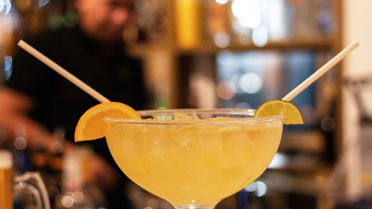A close up of a margarita with two straws and a slice of orange.