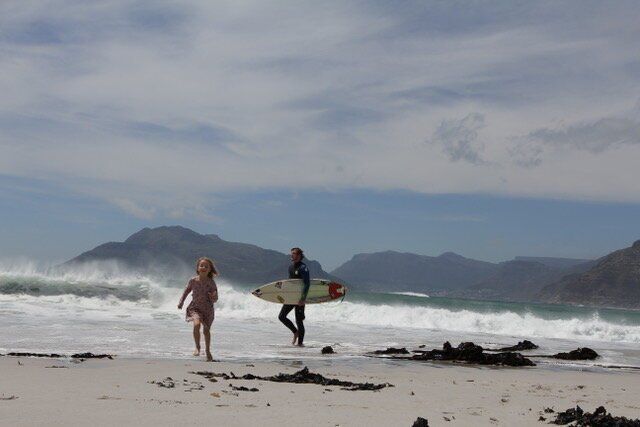 to personer, der bærer surfbrætter på en strand med bjerge i baggrunden