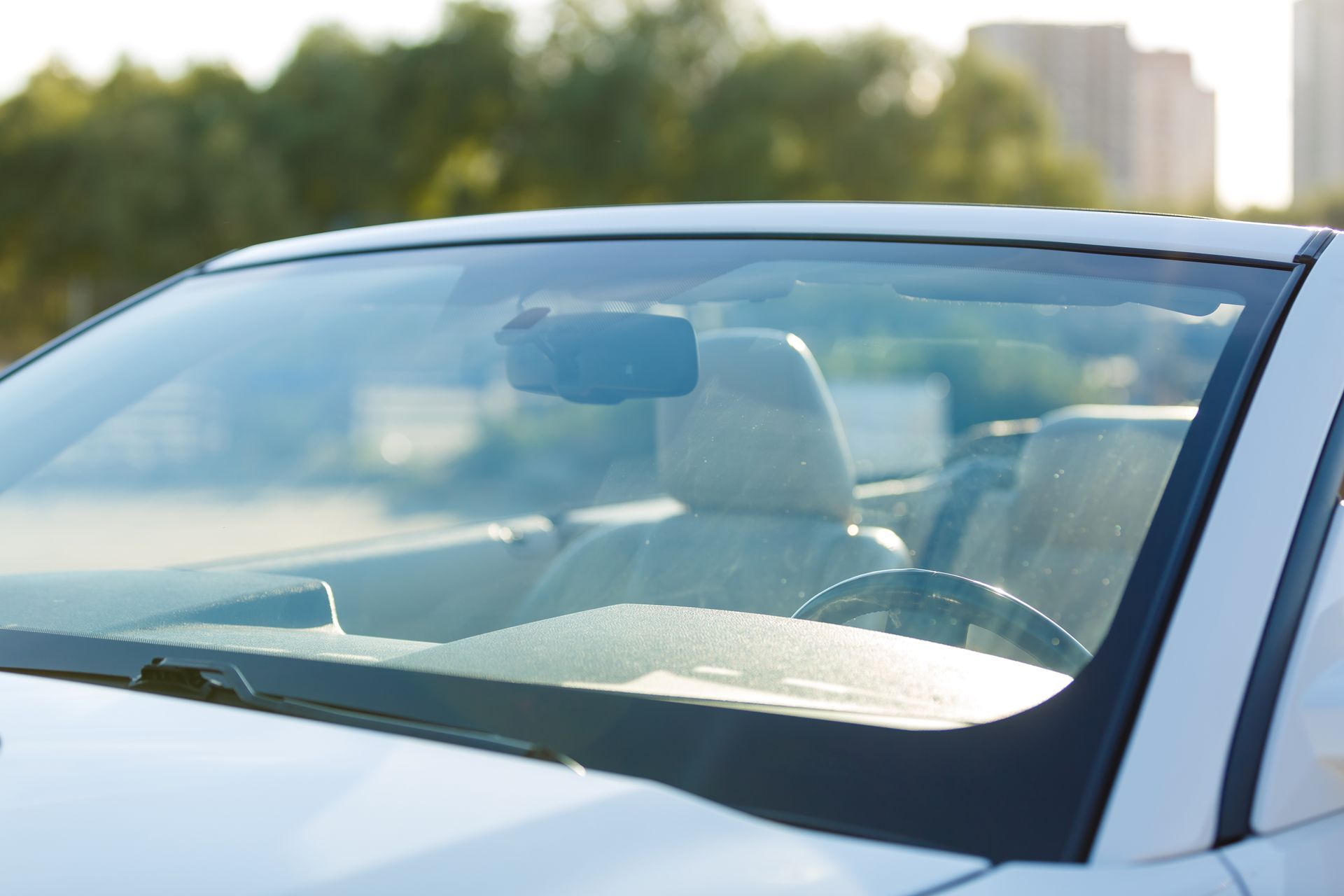 White convertible car interior, focus on windshield and steering wheel, sunny outdoor setting.