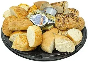 Bread rolls and sliced bread on a black serving tray with butter packets.