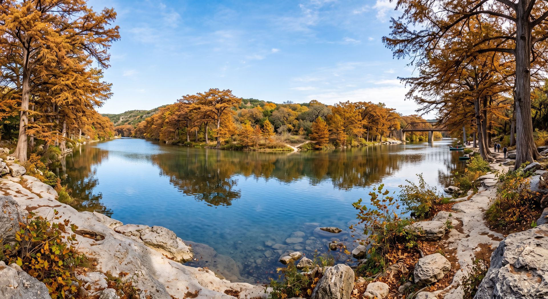 Autumn forest reflected in a calm lake, framed by rocky shoreline and blue sky