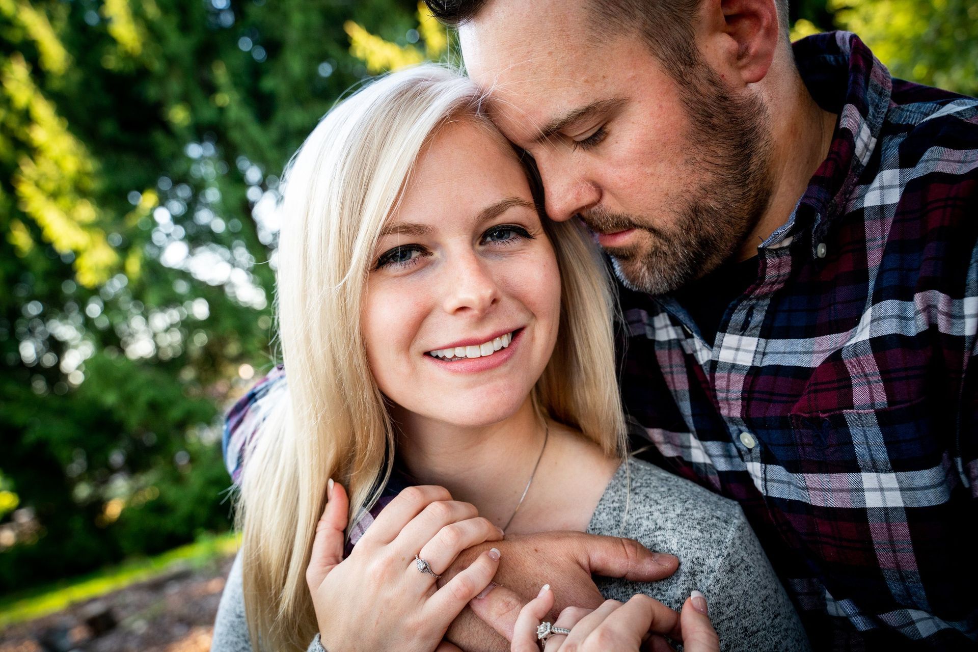 Couple embracing outdoors, woman smiling at camera, man with arm around her.