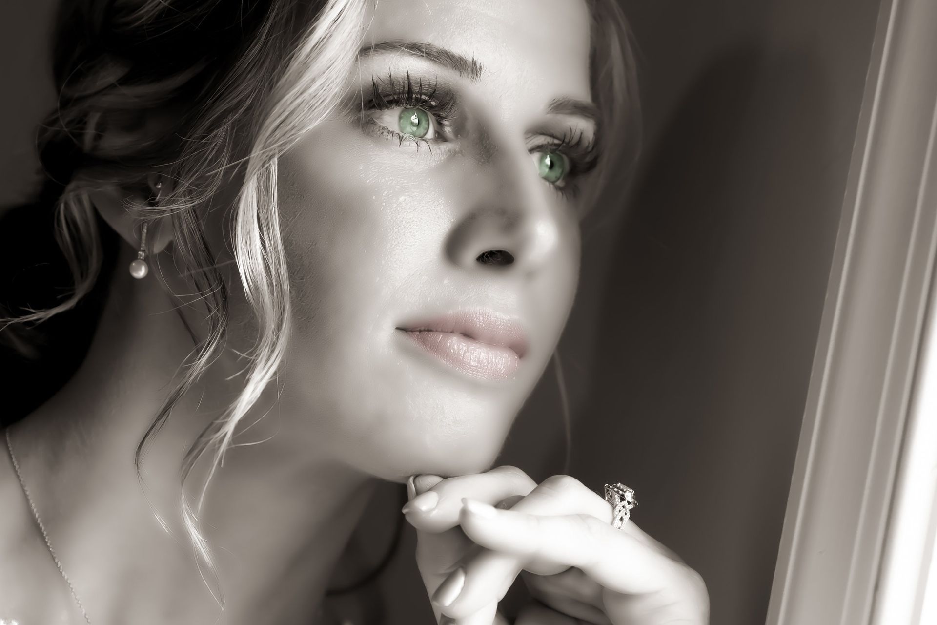 Blonde woman with green eyes gazes thoughtfully; hand on chin. Black and white, except for eyes.