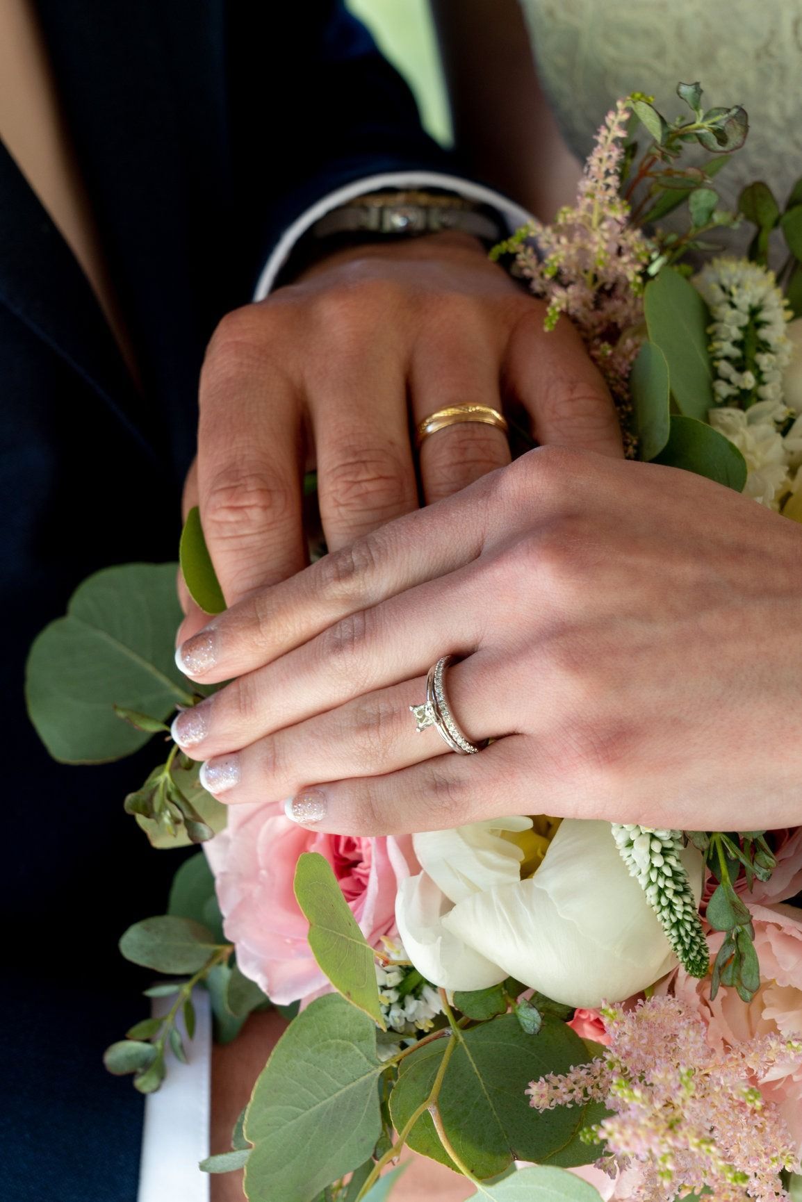 Hands with wedding rings holding a bouquet of flowers, close up.