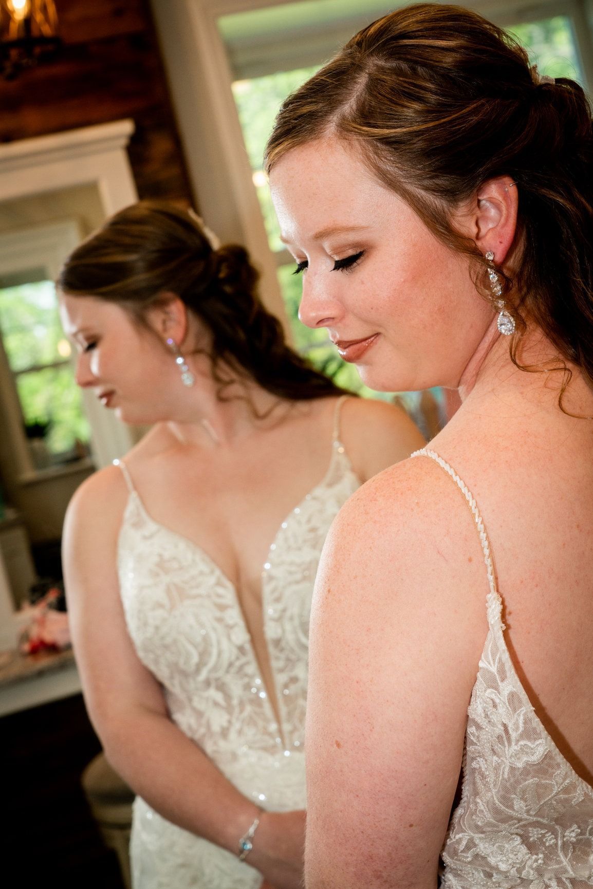 Bride in a wedding dress looking at herself in a mirror; natural light, light-colored dress.