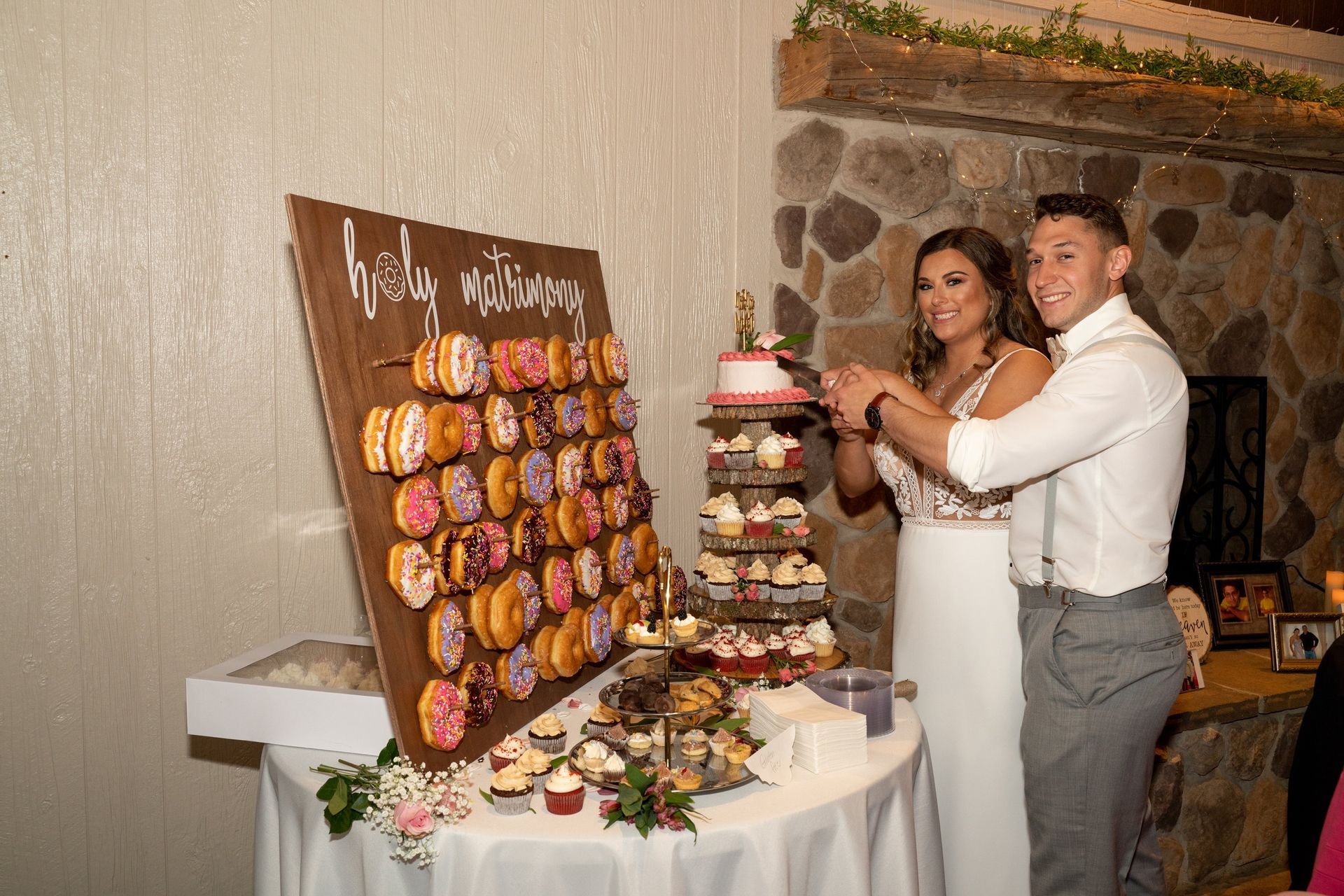 Bride and groom cutting a small cake near a donut wall.