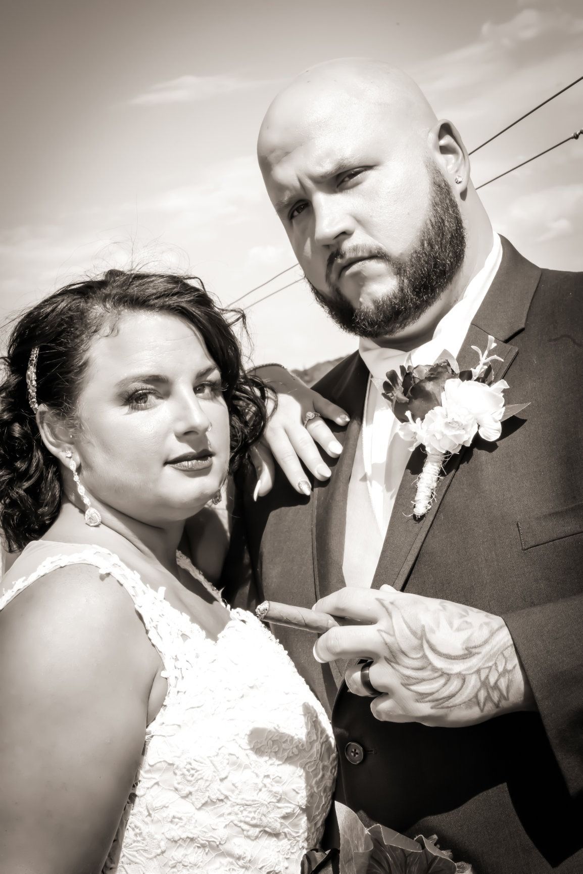 Bride and groom posing outdoors; bride in white lace dress, groom in suit. Sepia tone.