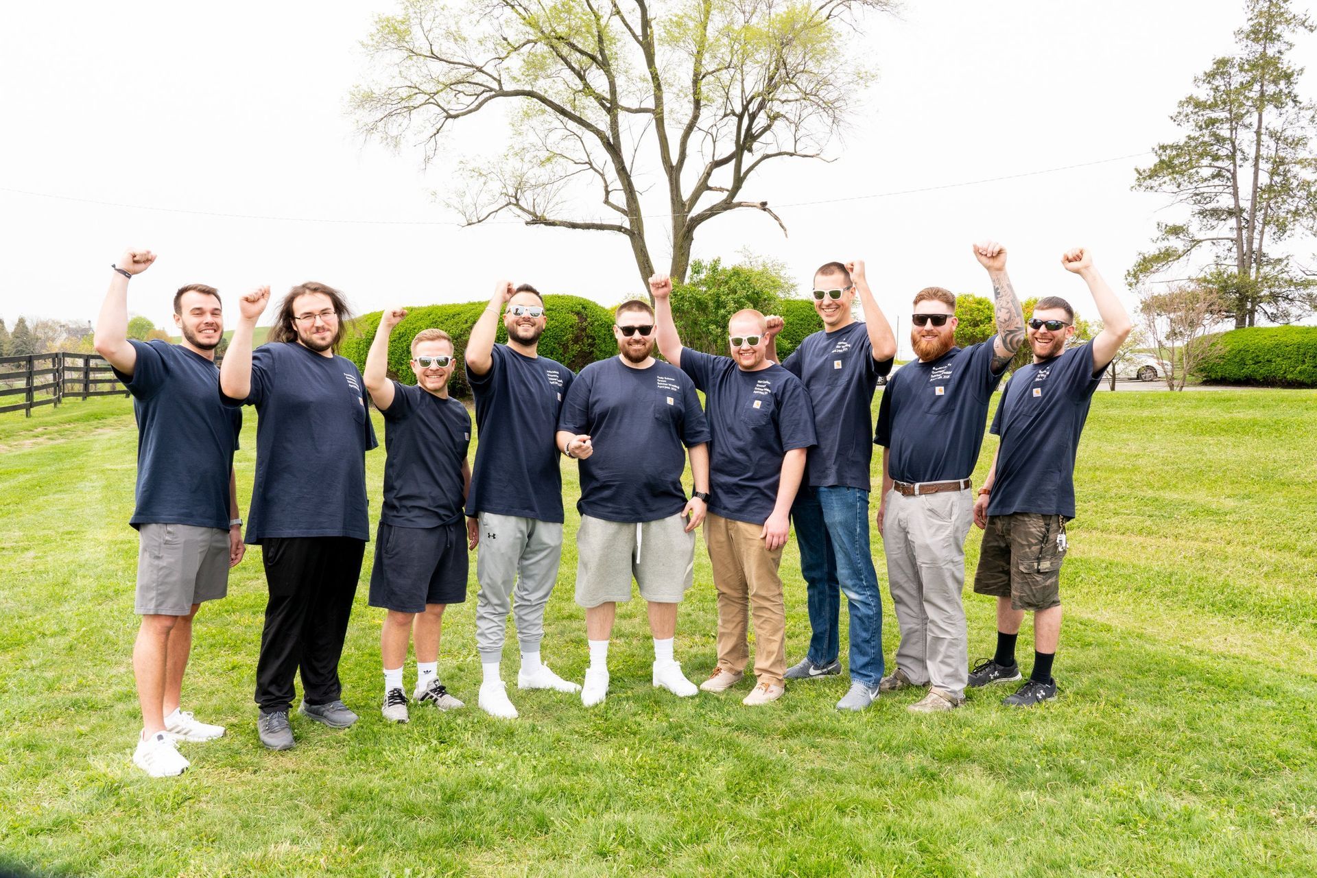 A group of ten men in blue shirts and various pants raising fists on a green lawn.