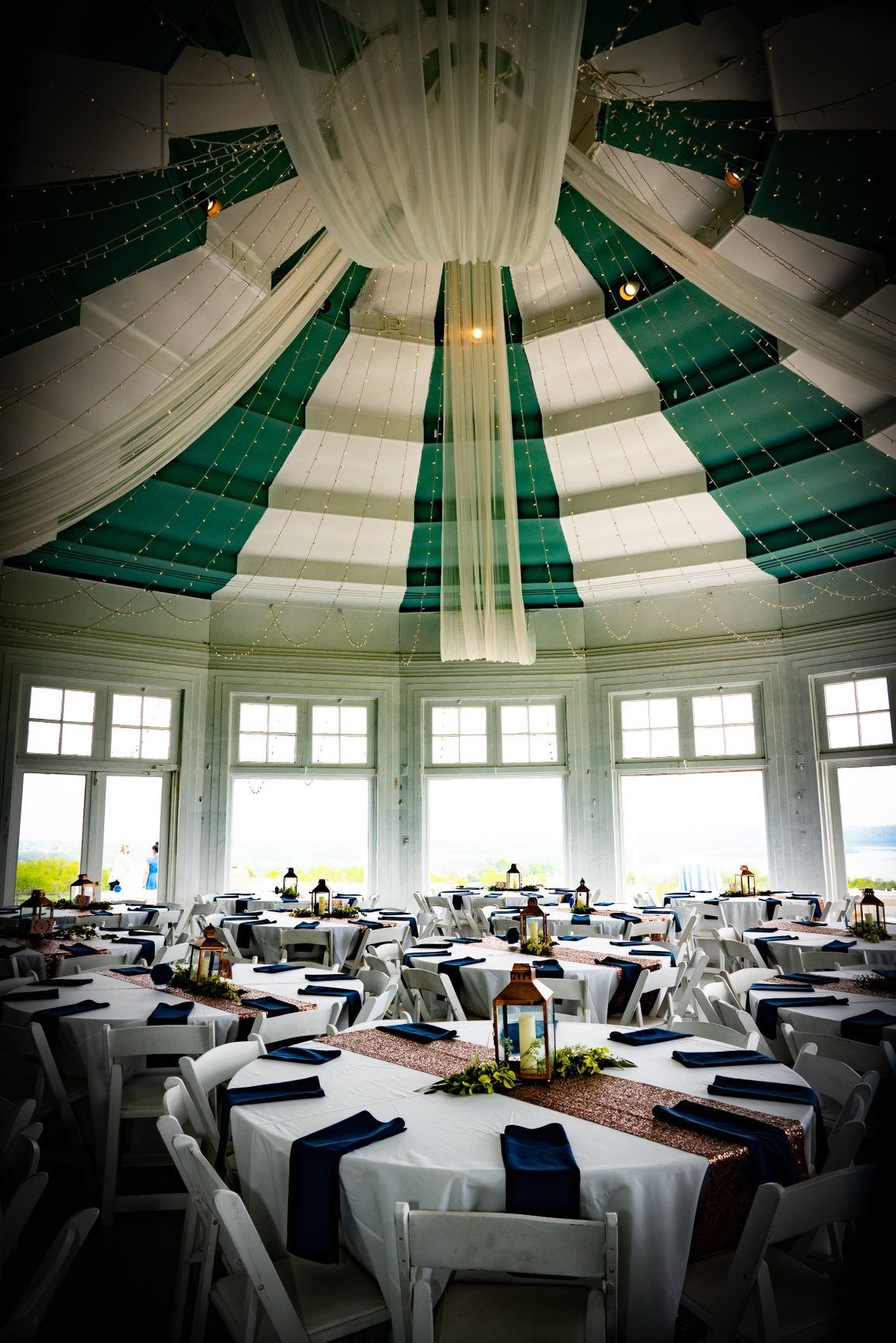 Wedding reception in a round room with tables set for guests. Green and white striped ceiling.