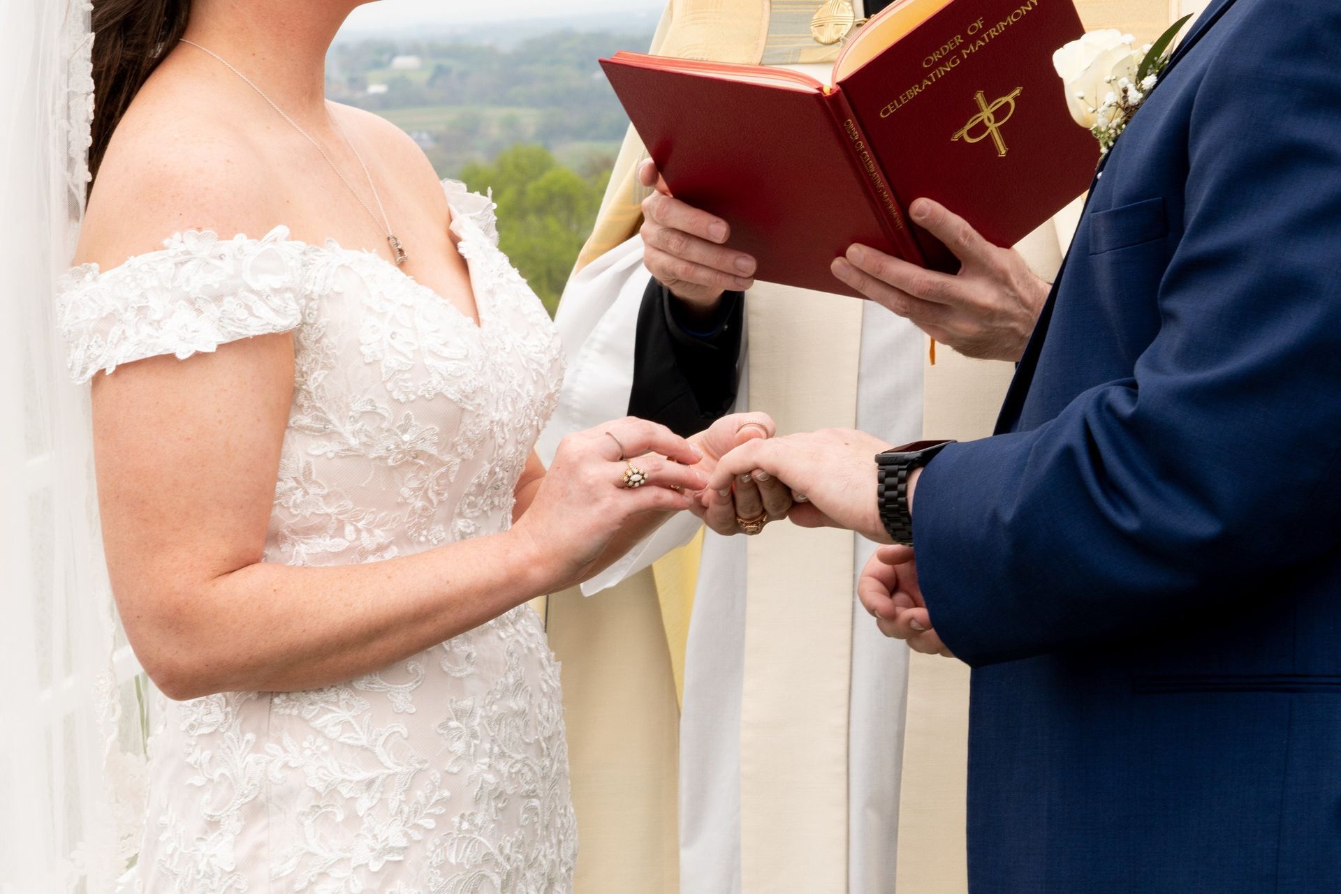 Bride and groom exchanging rings at an outdoor wedding ceremony, officiant holding a bible.