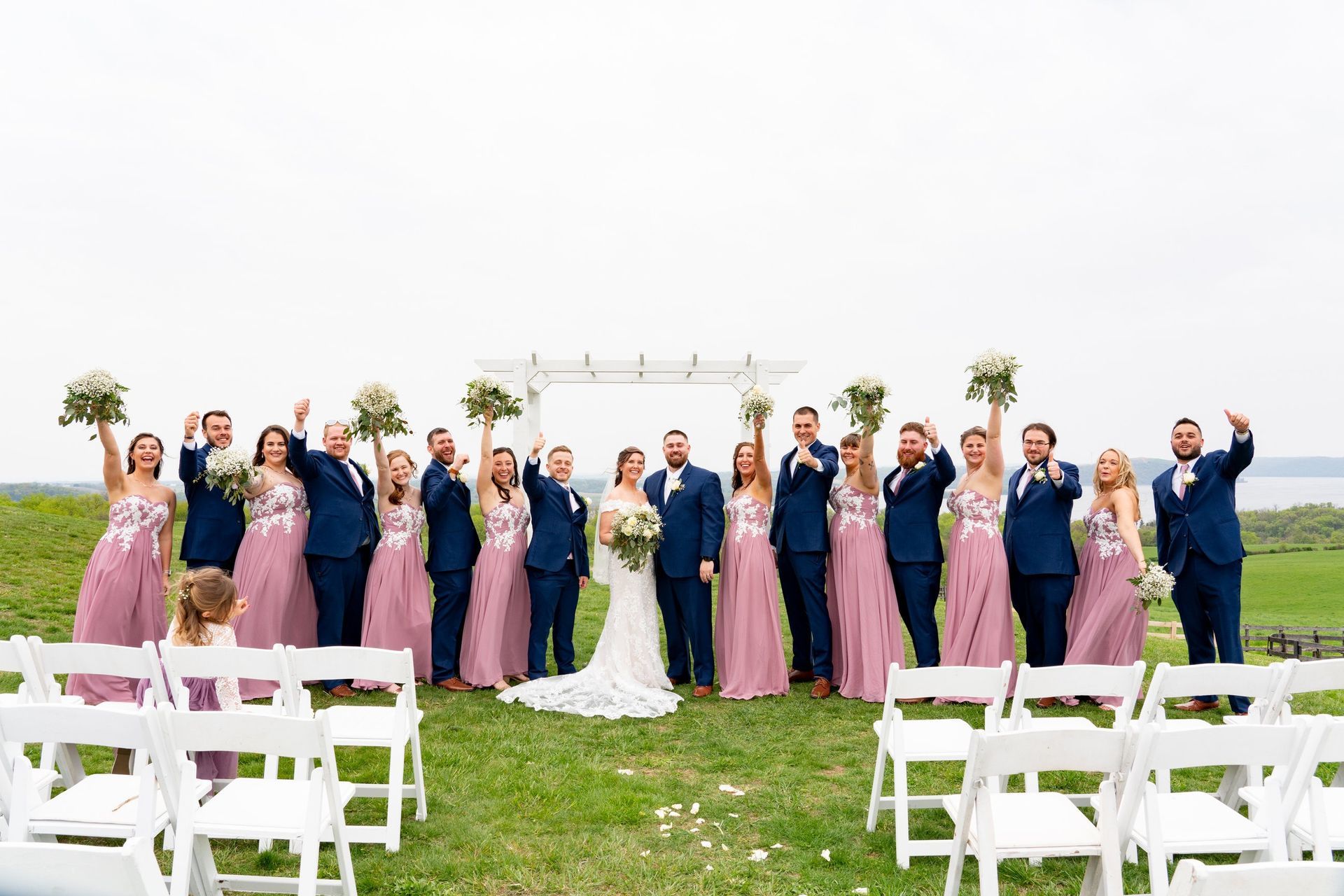 Wedding party celebrating outdoors; bride, groom, bridesmaids in pink, groomsmen in blue.