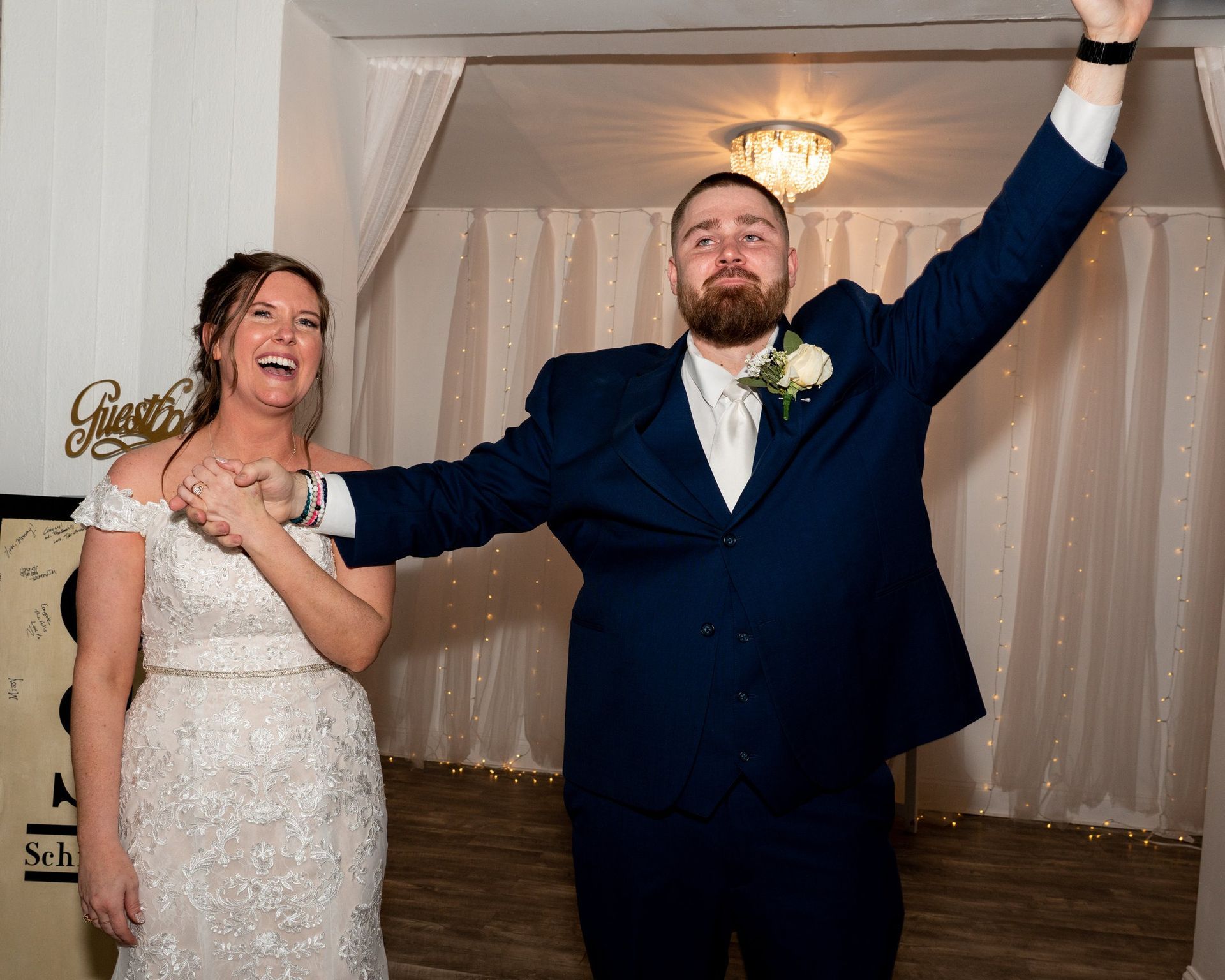 Newlyweds celebrating; bride laughs, groom raises arm in joyous celebration, doorway arch.
