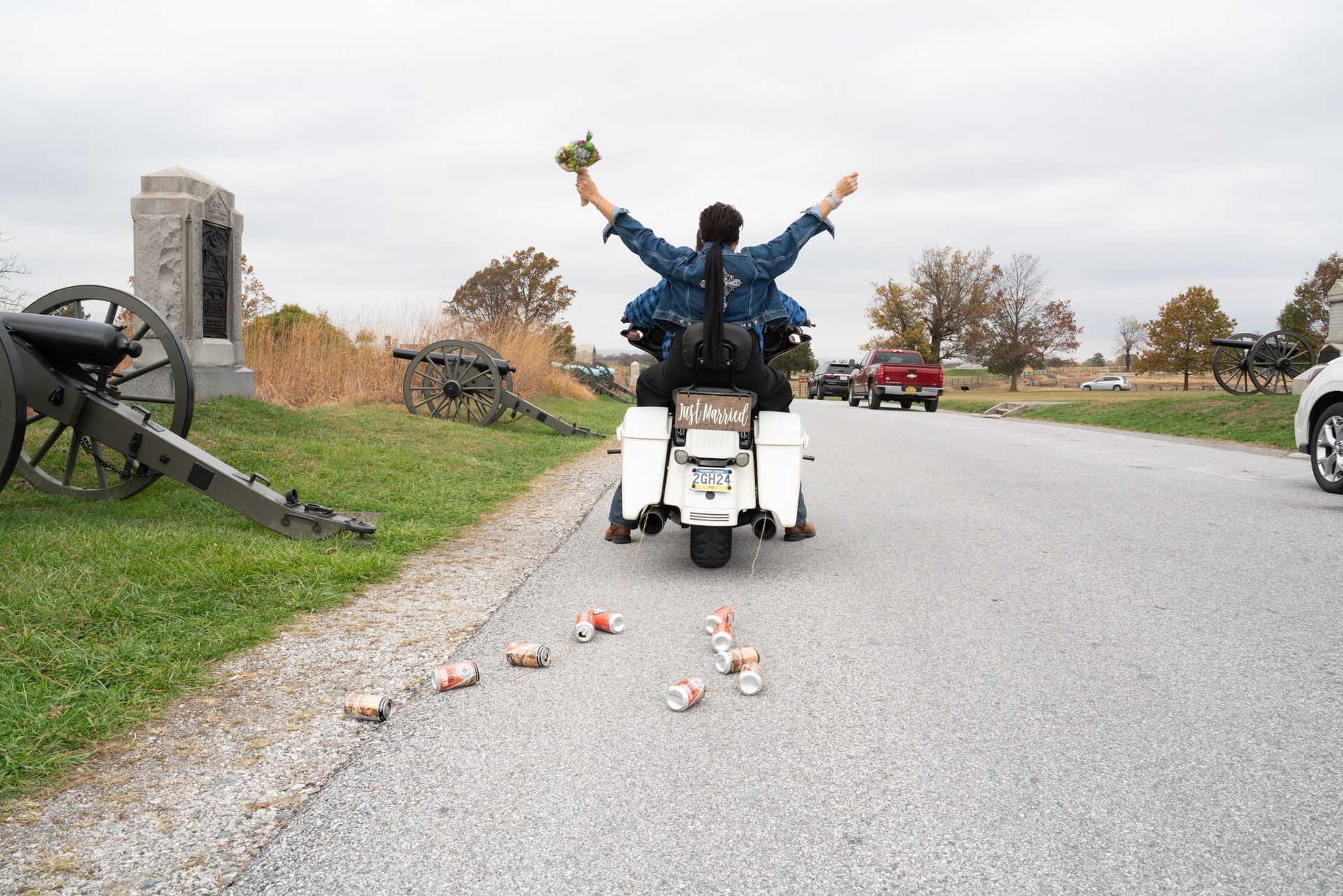 Person on a motorcycle with arms raised, surrounded by fallen objects on a road next to a monument and cannons.