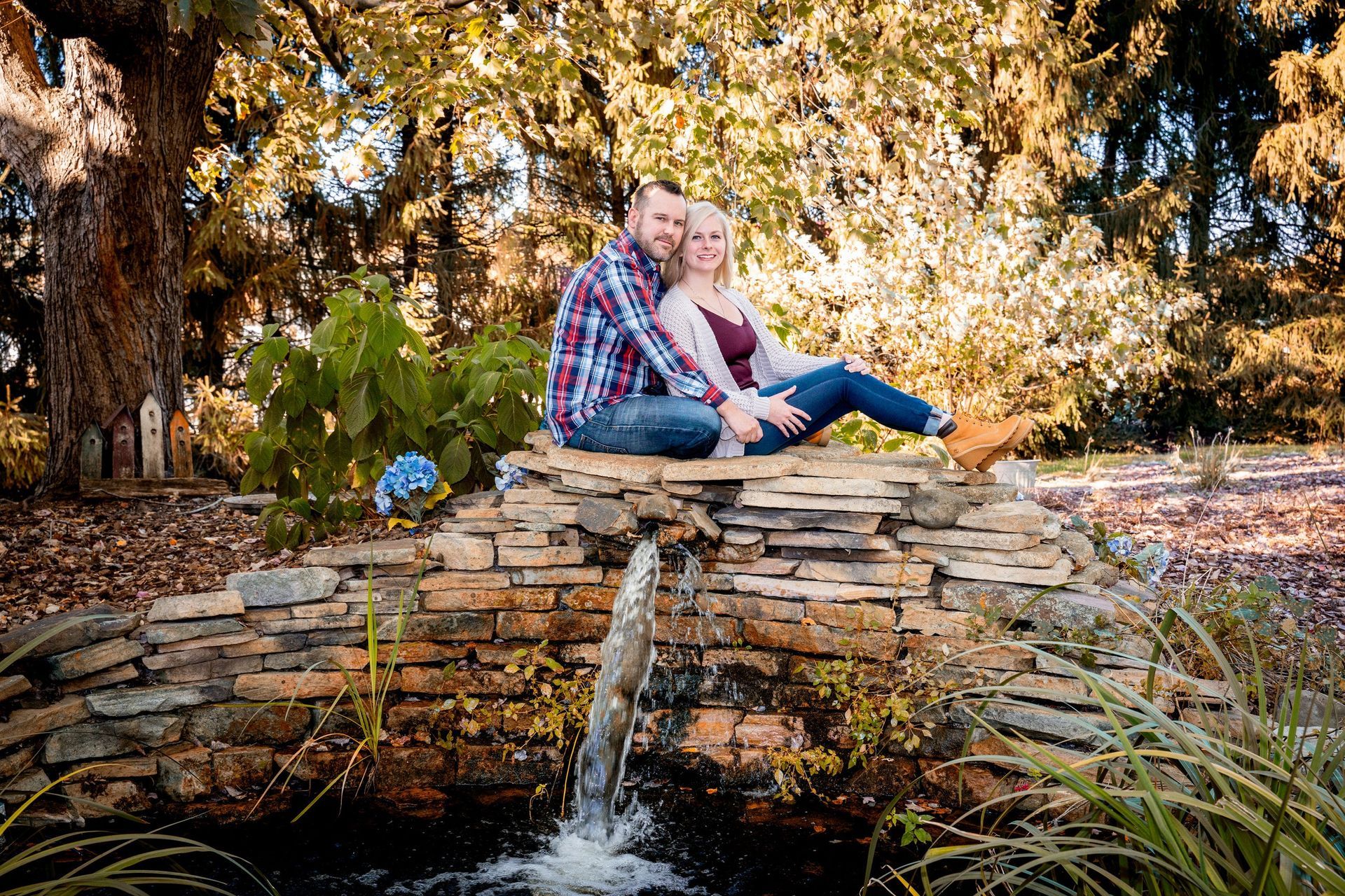 Couple sitting on a stone structure with a water fountain, in a park setting.