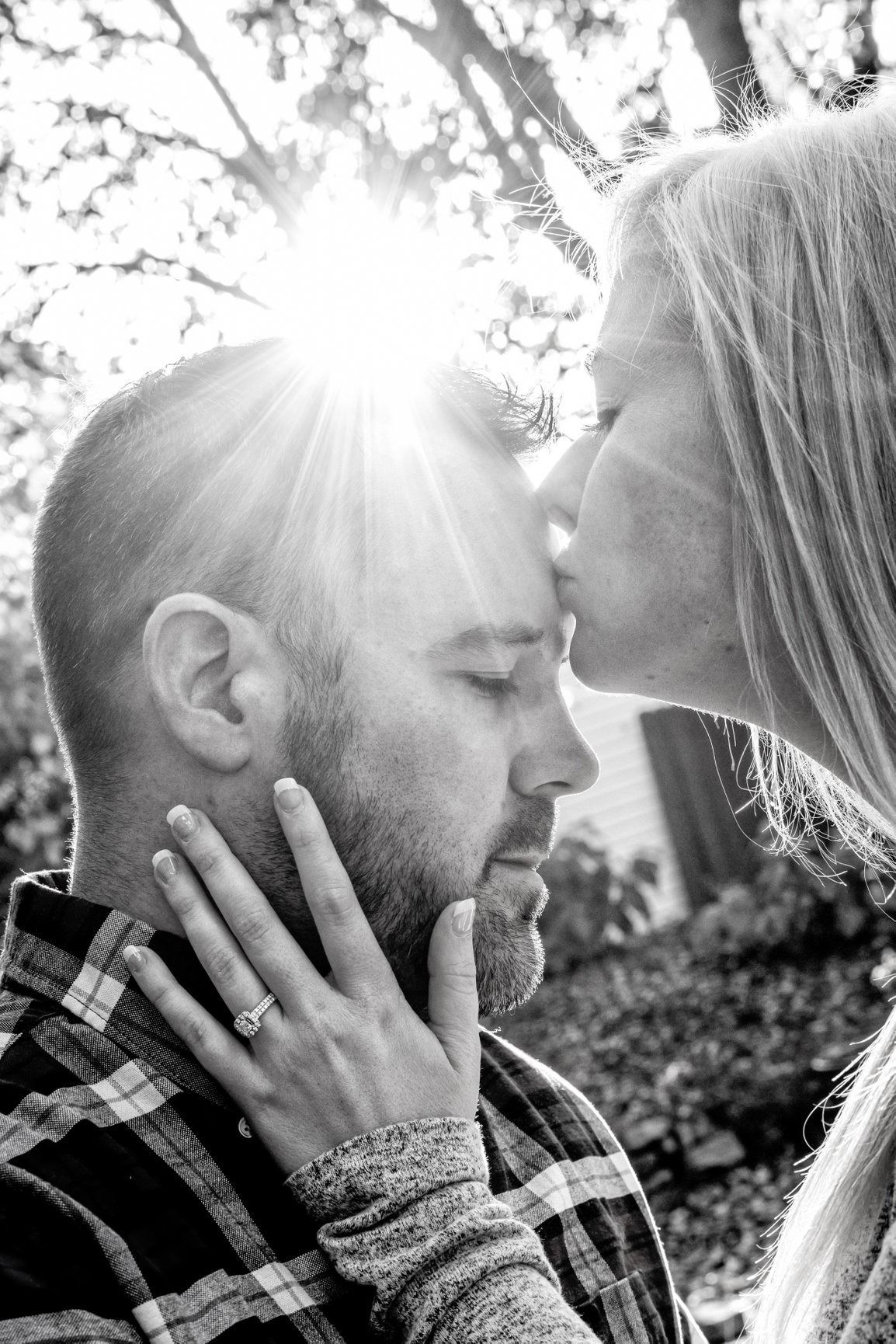Woman kissing man's forehead; sunlight flares around them. Man's eyes closed, woman's hand on his face.