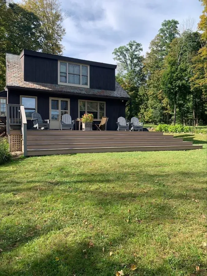 A black house with a large deck and chairs in front of it.