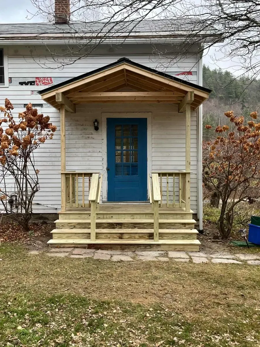 A white house with a blue door and a wooden porch.