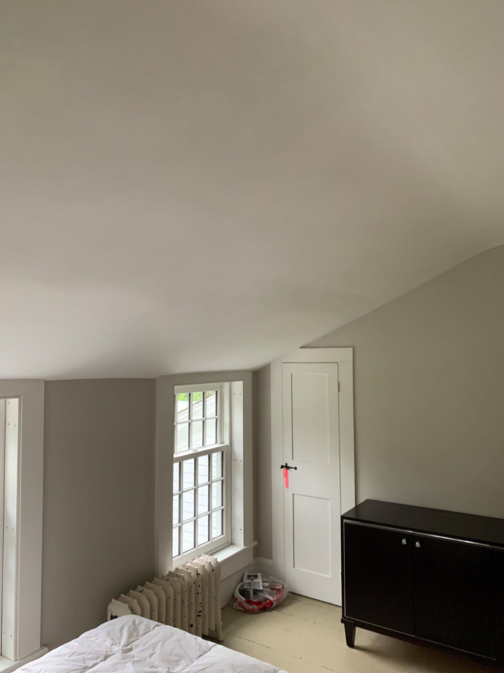 A bedroom with a bed , dresser , window and radiator.