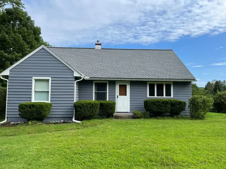 A small house with a gray siding and a white door is sitting on top of a lush green field.