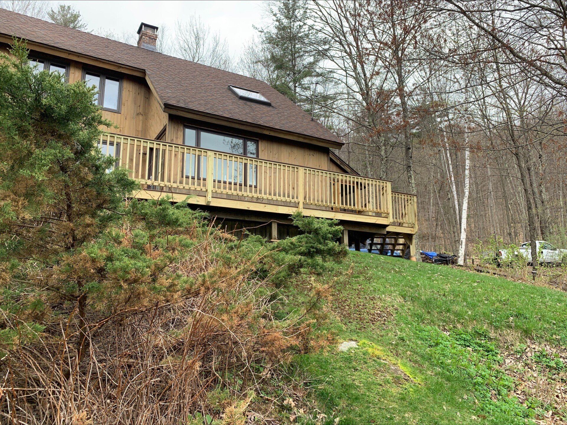 A house with a wooden deck is sitting on top of a grassy hill.