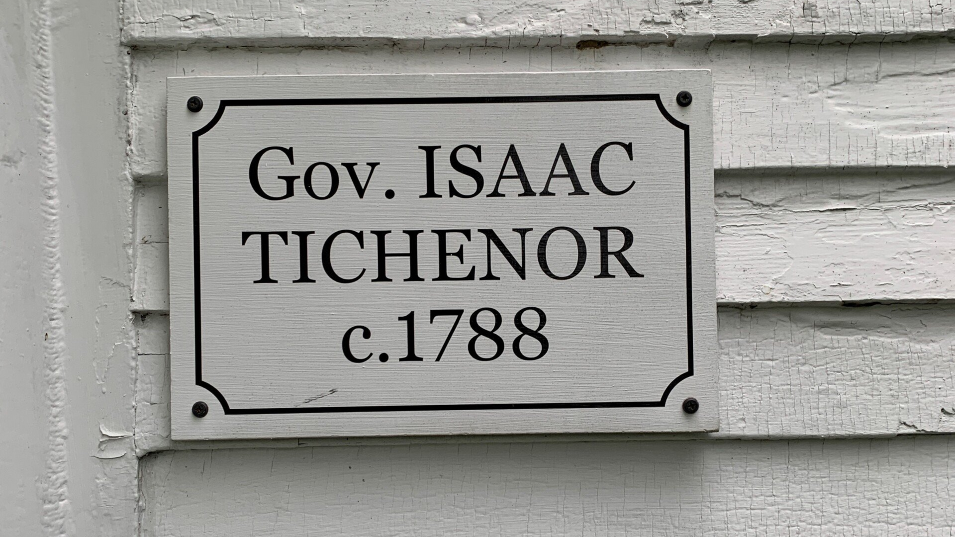 Plaque reading “Gov. ISAAC TICHENOR c.1788” on a gray wooden building