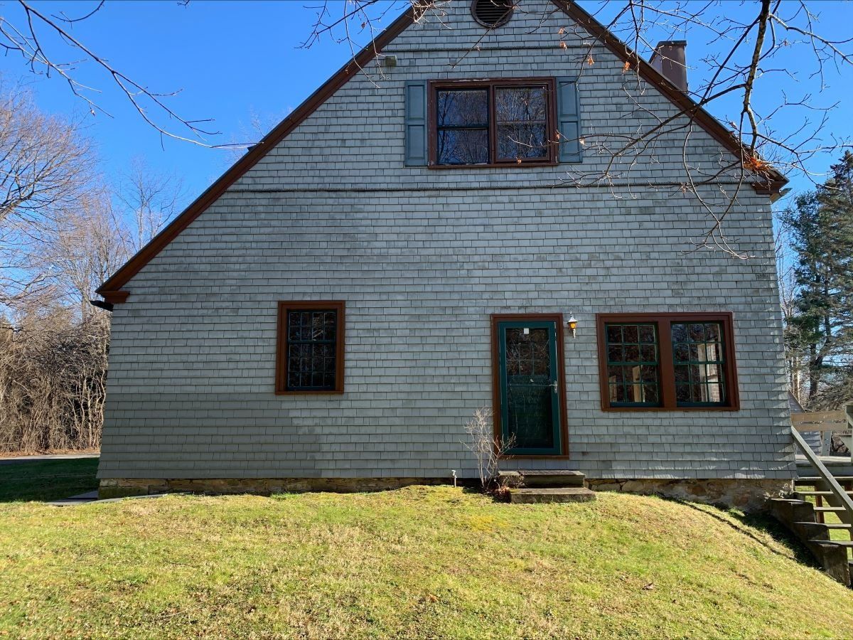 A white house with a green door and windows is sitting on top of a grassy hill.