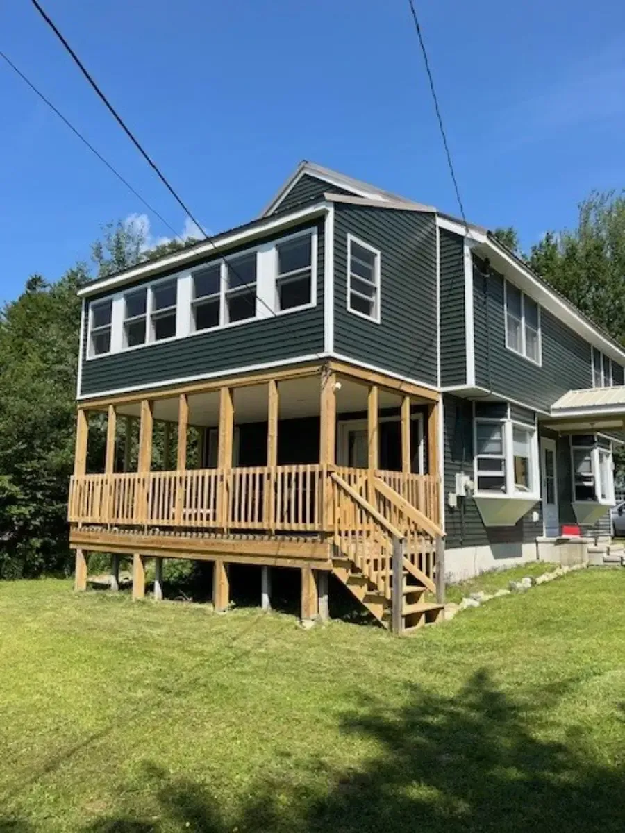 Green house with a wooden porch and stairs on a grassy lawn under a blue sky