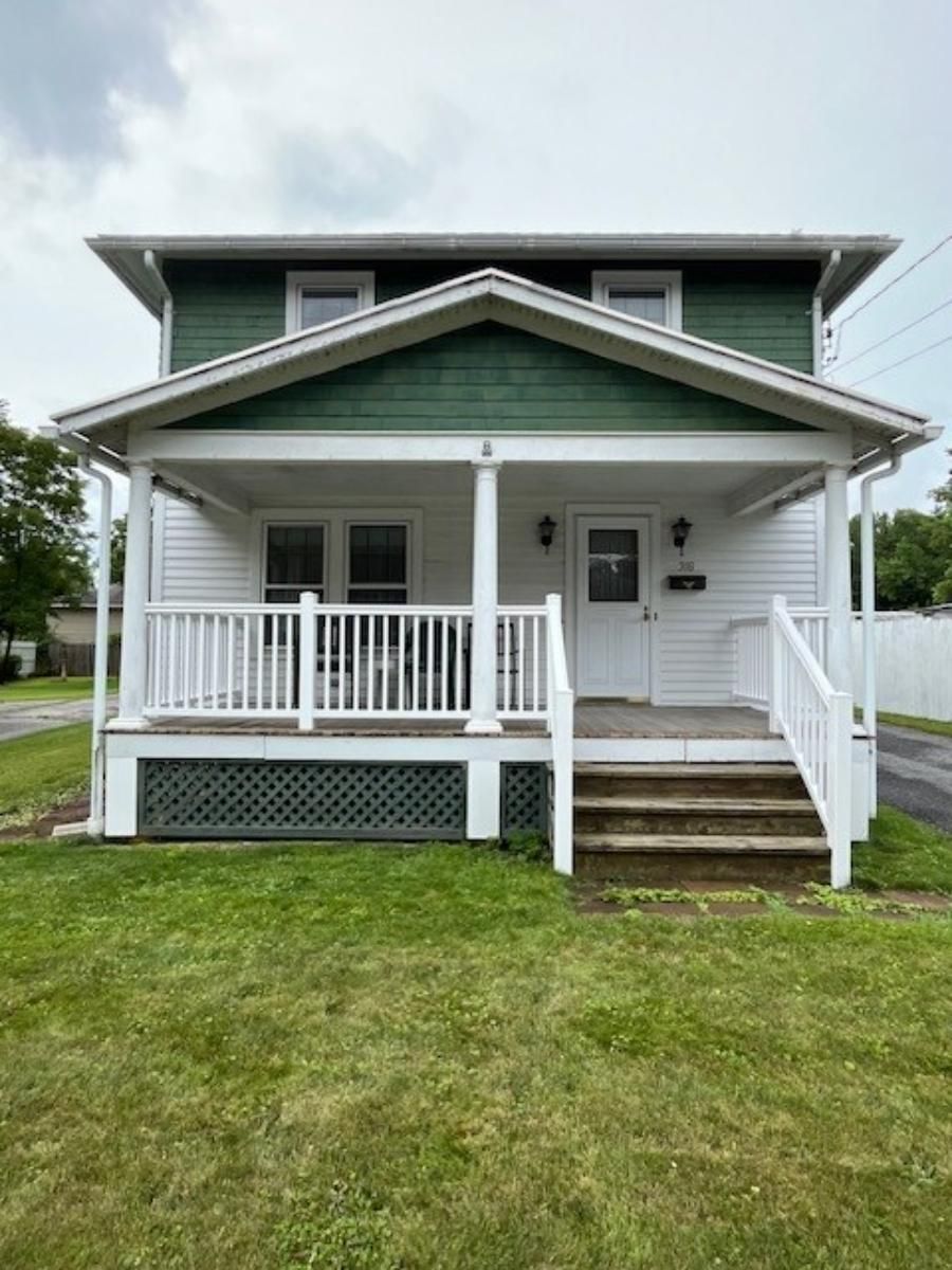 A green and white house with a porch and stairs.