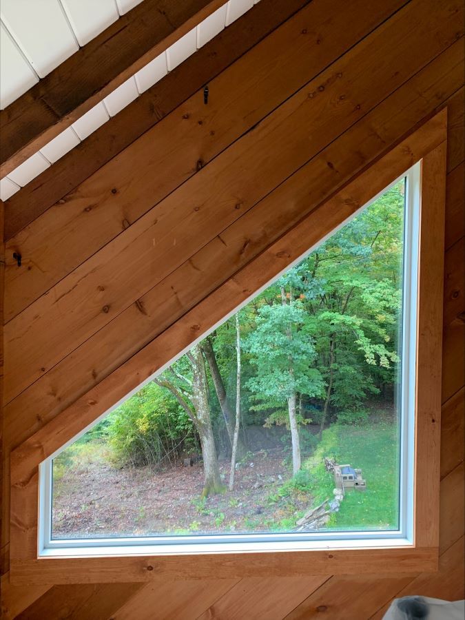 A triangle window with a view of trees in a wooden house
