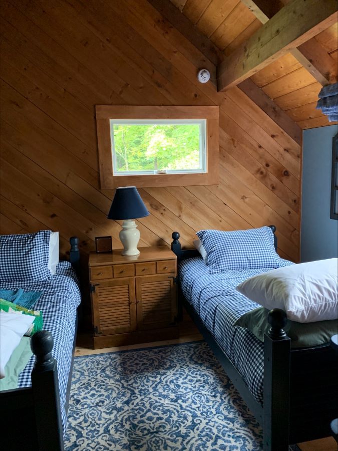 A bedroom with two beds , a nightstand , a lamp and a window.
