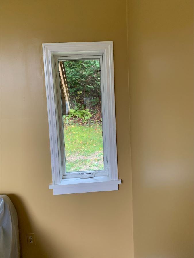A large mirror is hanging on a yellow wall next to a window.