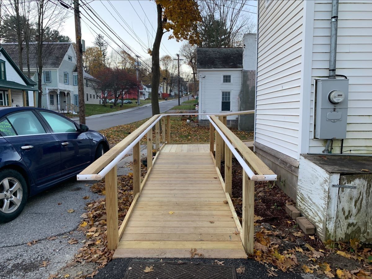 A blue car is parked next to a wooden ramp leading to a house.