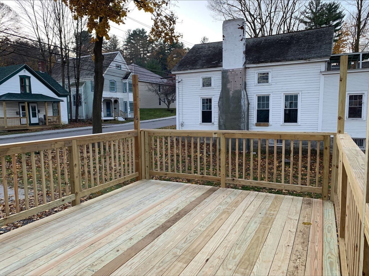 A wooden deck with a railing in front of a white house.
