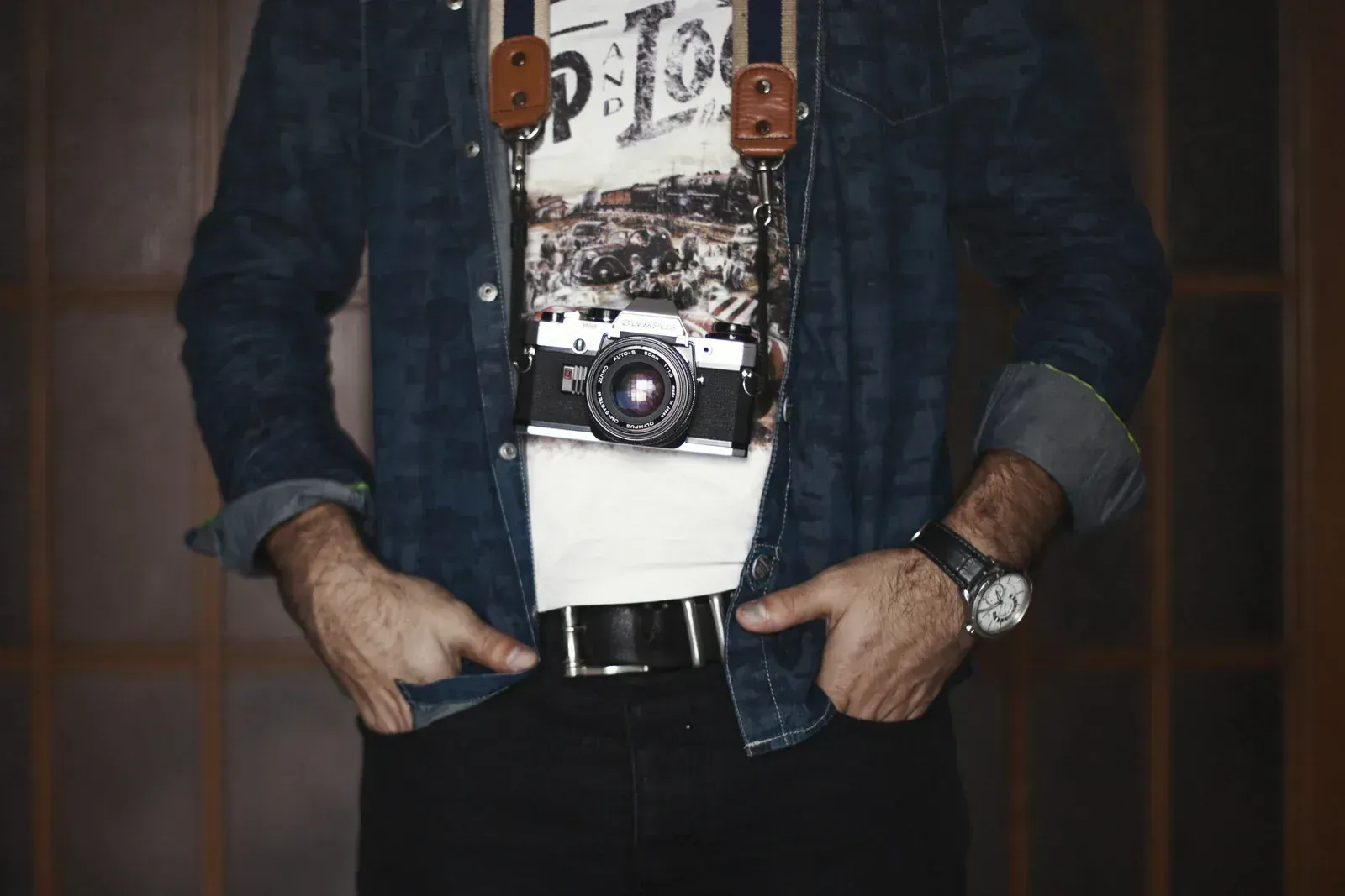 Person in denim jacket and jeans stands with hands in pockets, wearing a graphic T-shirt and camera print.