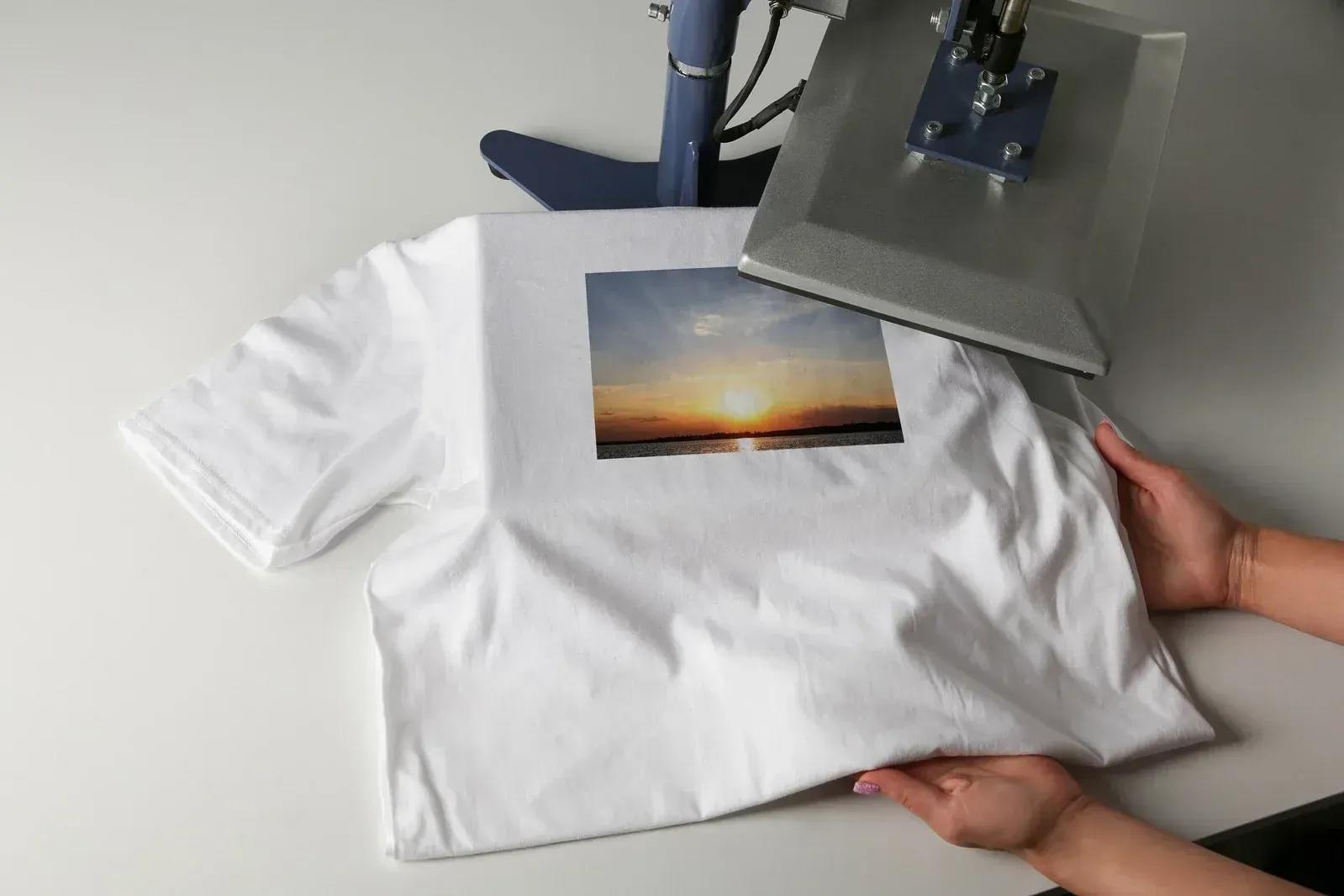 White T-shirt with a sunset photo print being held under a heat press for transfer printing