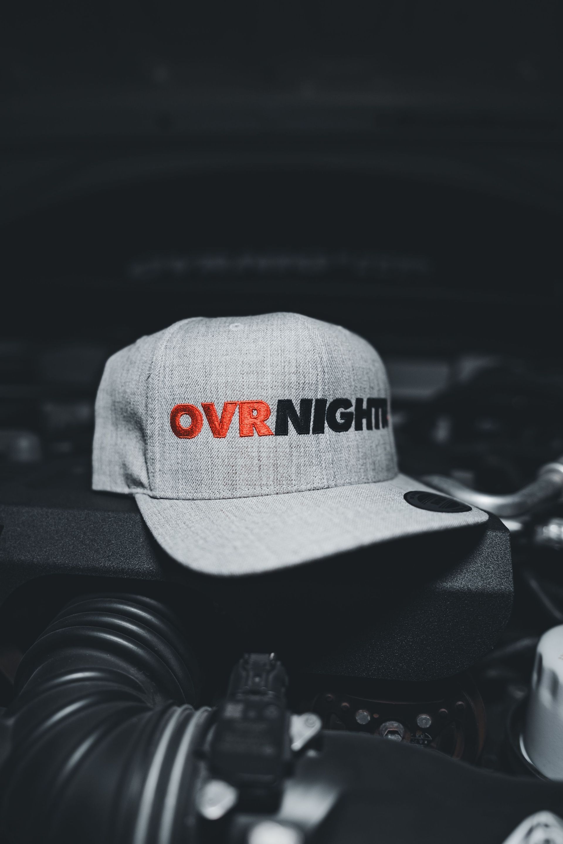 Gray cap with “OVN NIGHTS” logo resting on a black engine component in a dark setting