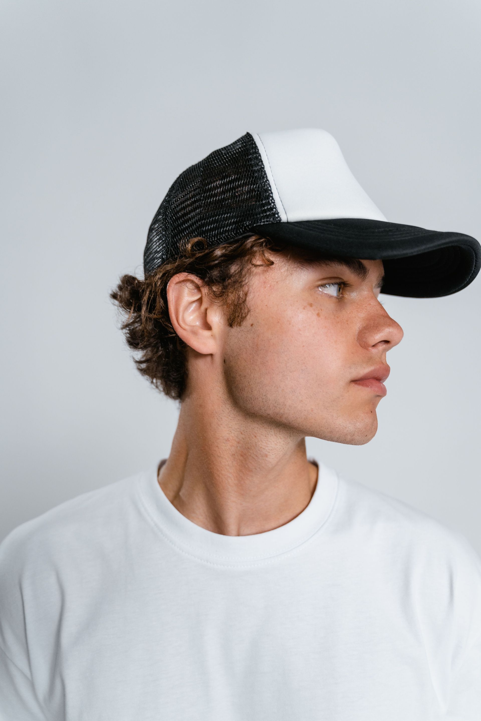 Person in a white T-shirt and black-and-white cap, looking to the right against a gray background