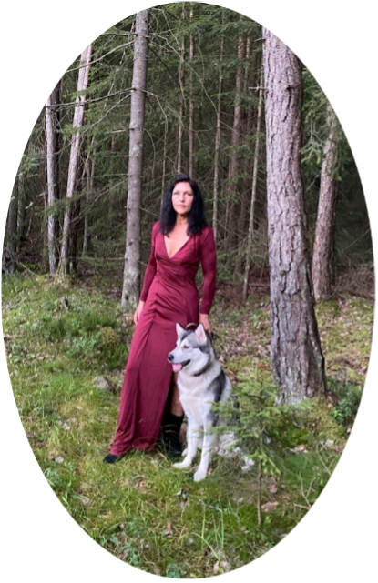 A woman in a red dress is standing next to a husky dog in the woods.