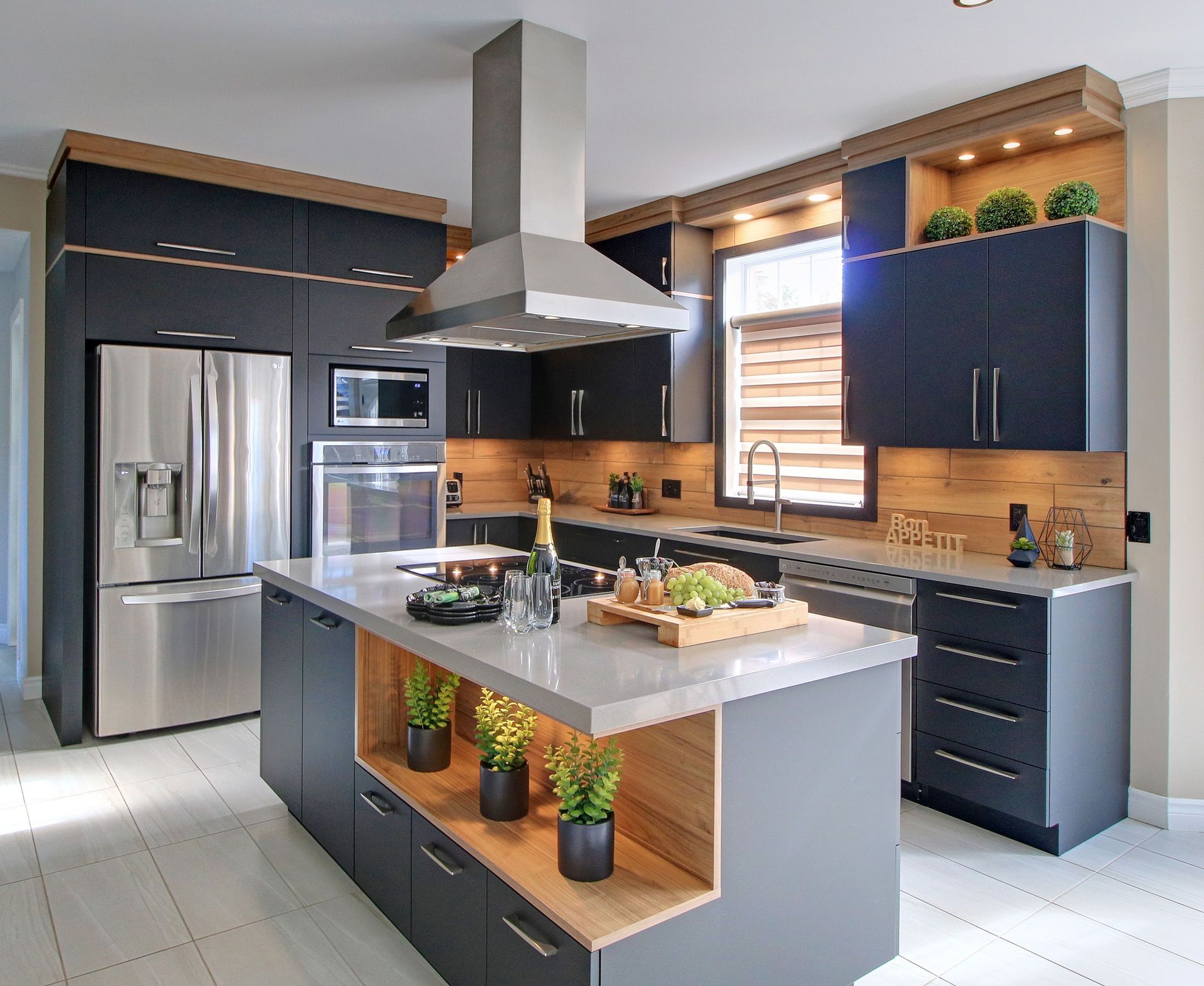 Cuisine moderne avec armoires gris foncé, touches de bois clair, un grand îlot central, des appareils électroménagers en acier inoxydable et un sol carrelé.